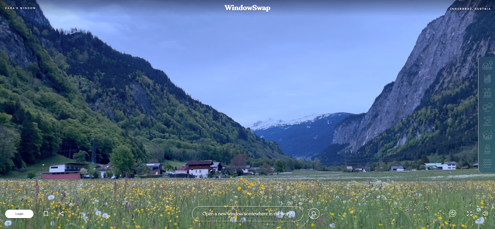 Point of view from a windowsill shows a serene small farm nestled between a wildflower meadow and snow-capped mountain peaks.