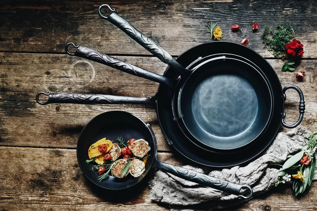 Cast iron pans on a wooden surface, arranged with home good and food