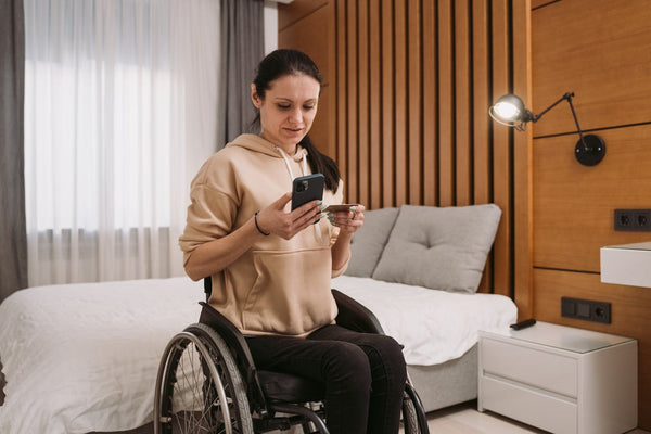 A woman sitting on her wheelchair while using her mobile phone and holding a credit card.