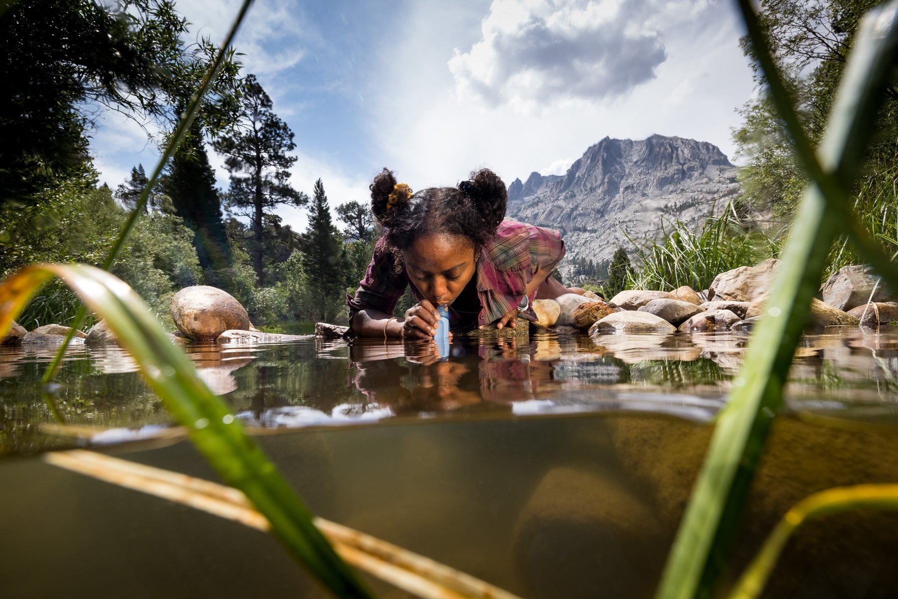 A woman drinks water from a stream through a LifeStraw.