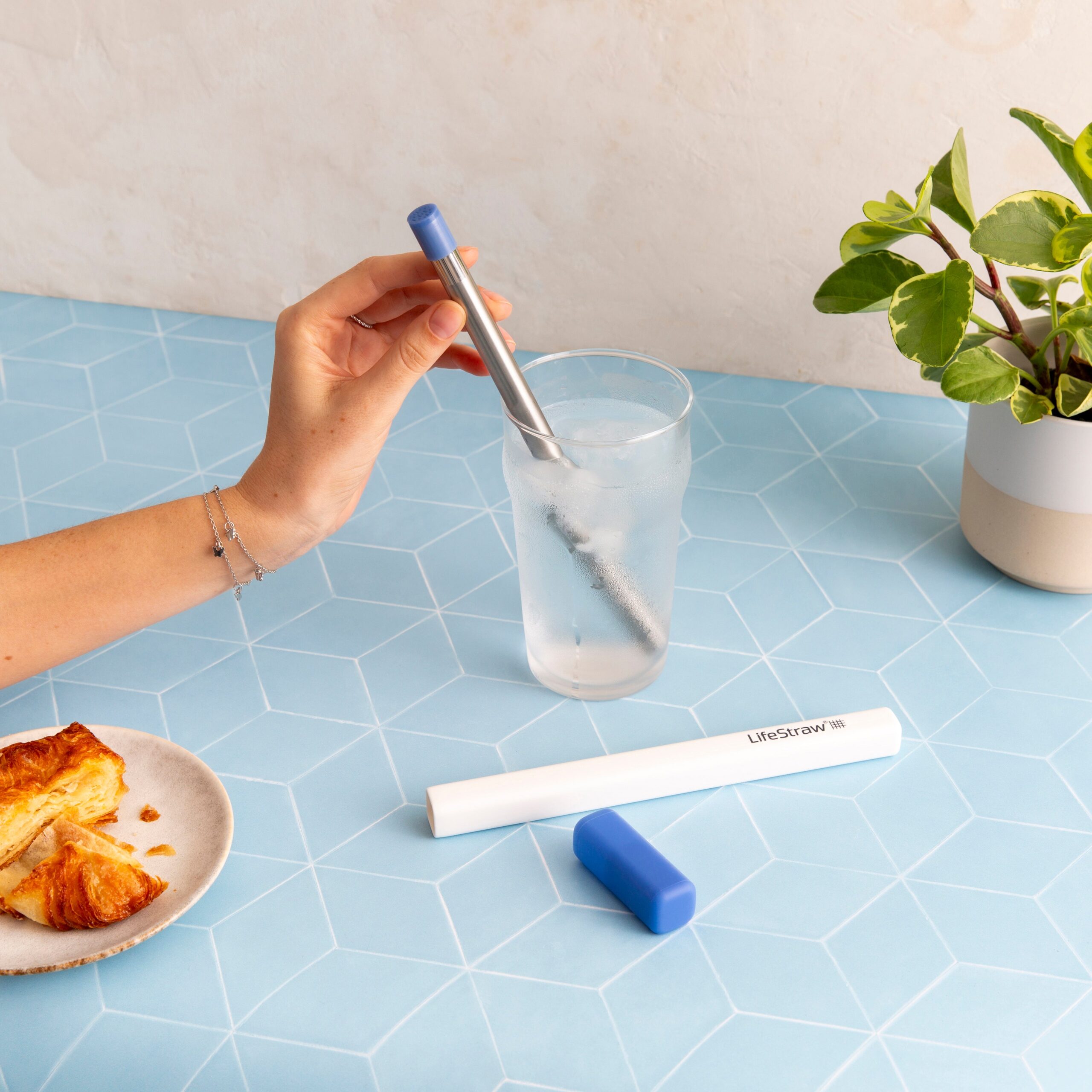 LifeStraw’s new Sip straw in a glass of water, with a croissant and plant on the table