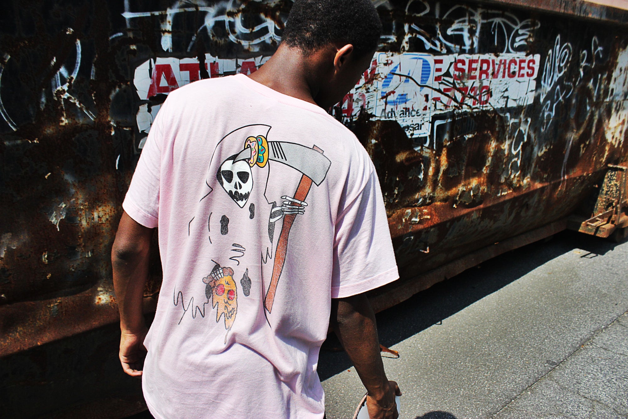 A young person photographed from behind wears a graphic tee and skates in an alley