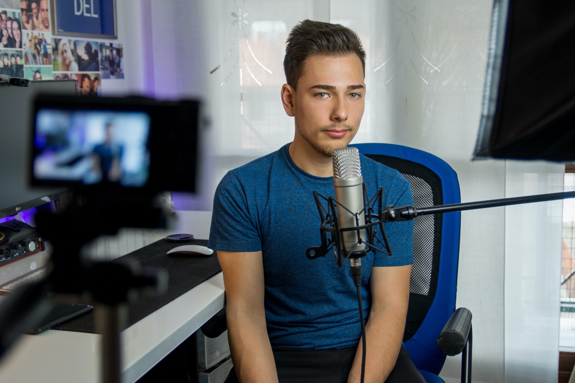 A young person sits in front of a computer and a microphone