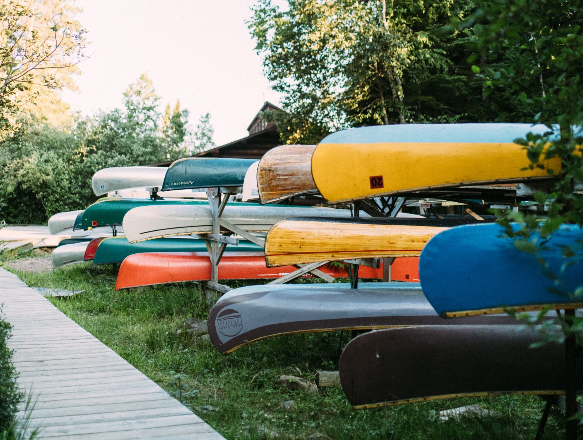 Stacks of canoes are lined up on racks next to a boardwalk