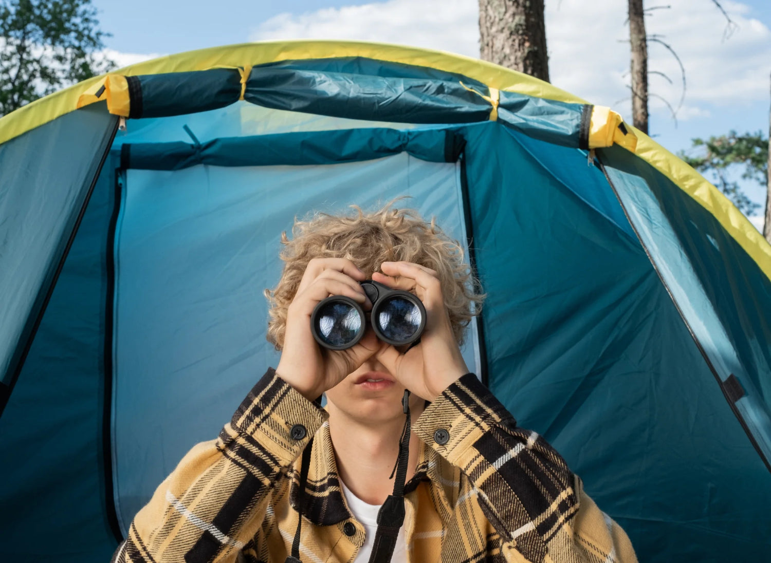 A person looks through binoculars in a camp setting