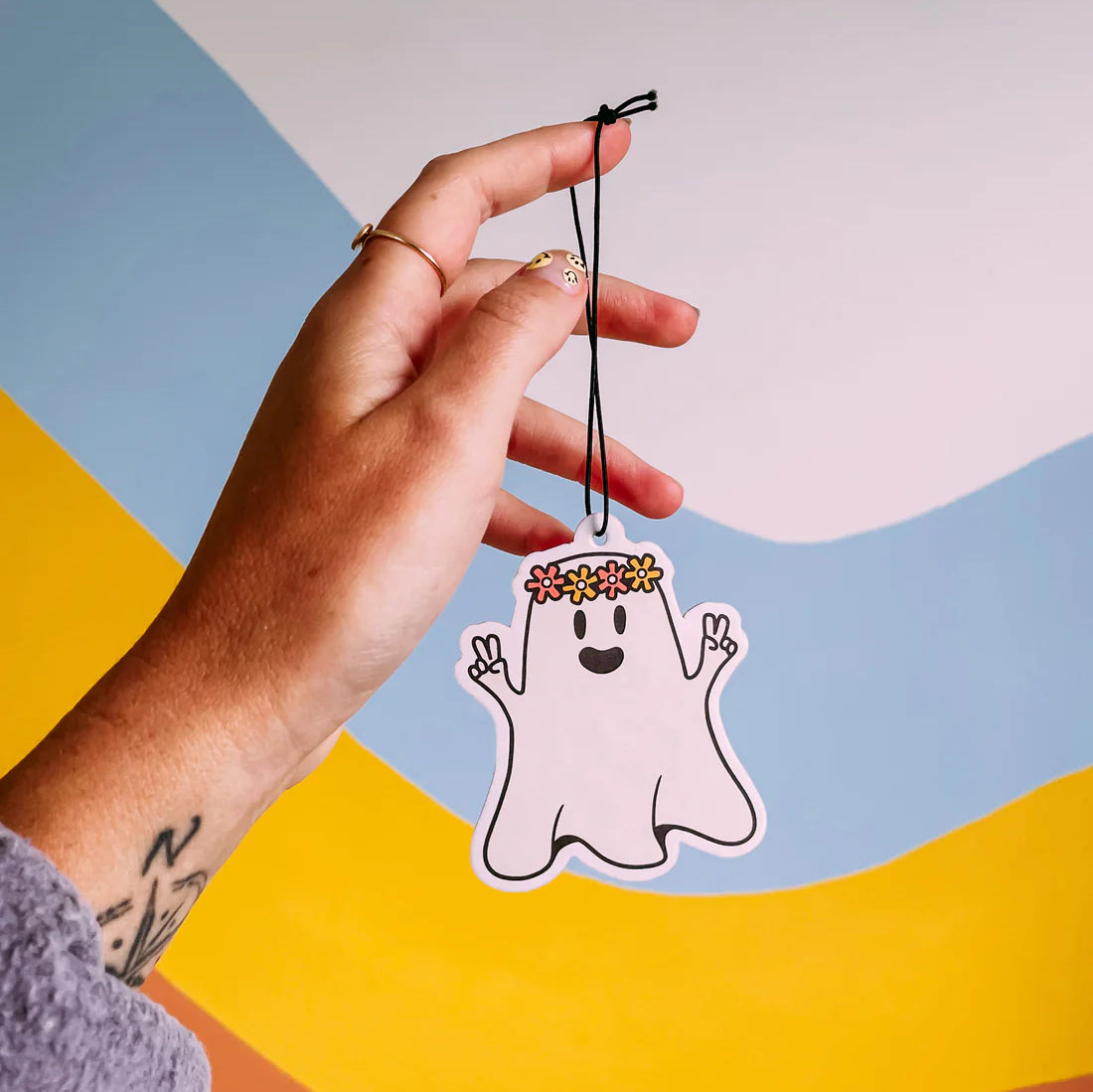 A hand holds up a car air freshener in a ghost design
