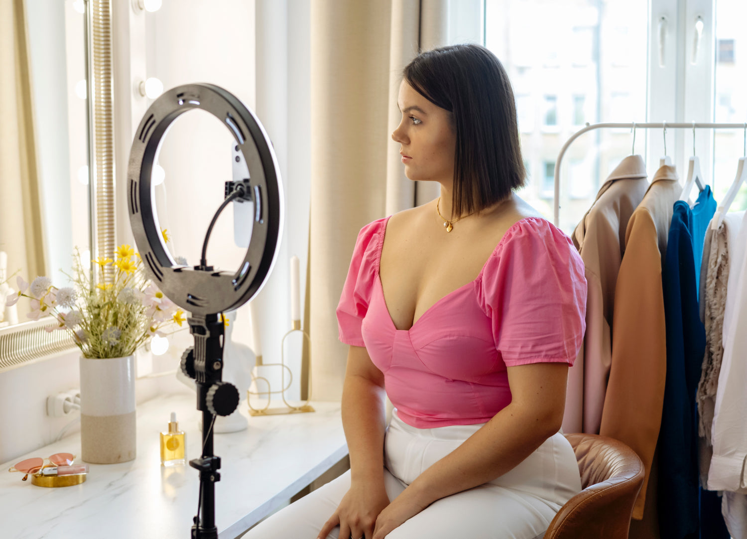 An influencer sits in front of a ring light recording herself on a phone to make money online