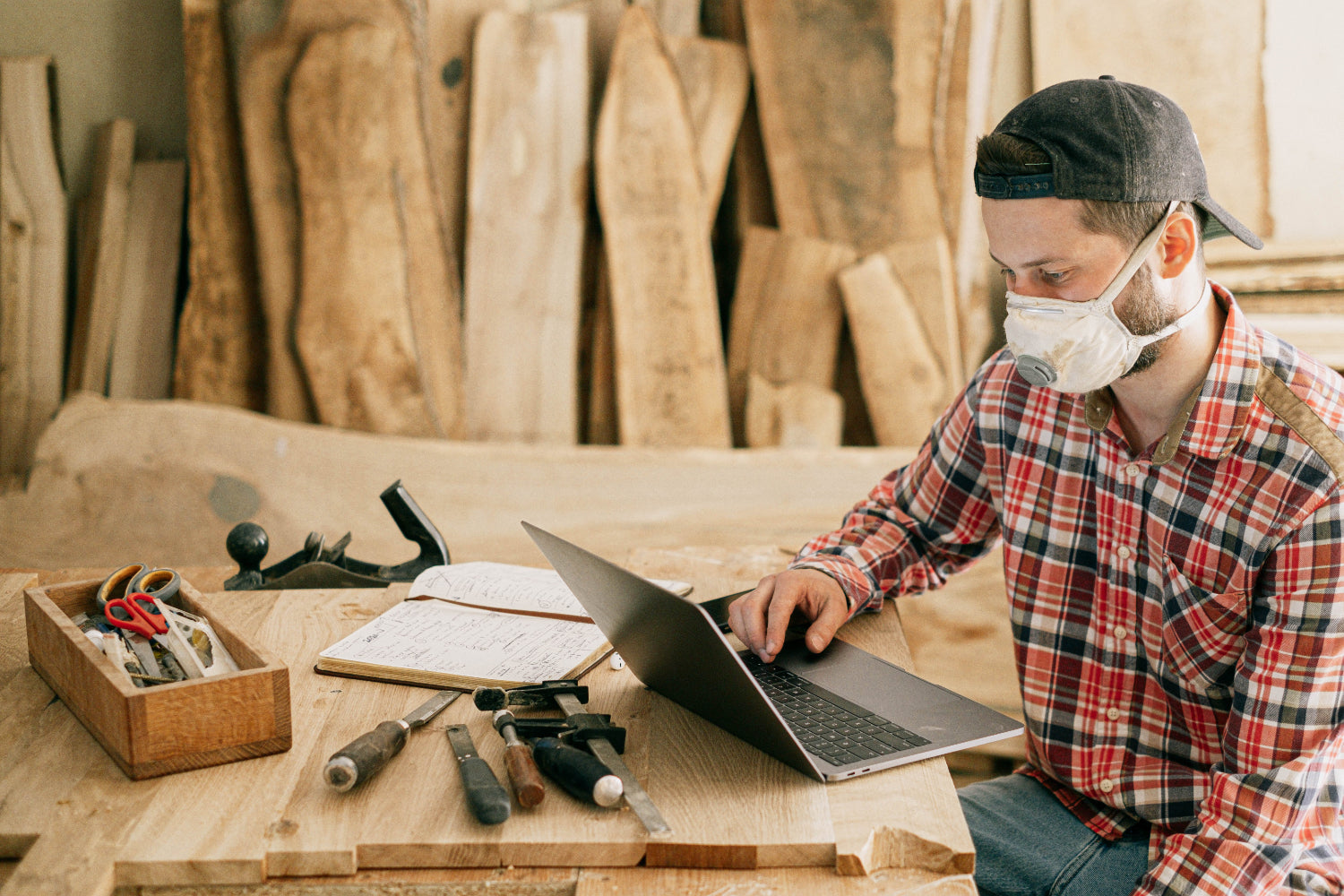 A person makes money online on their laptop in a woodworking shop setting