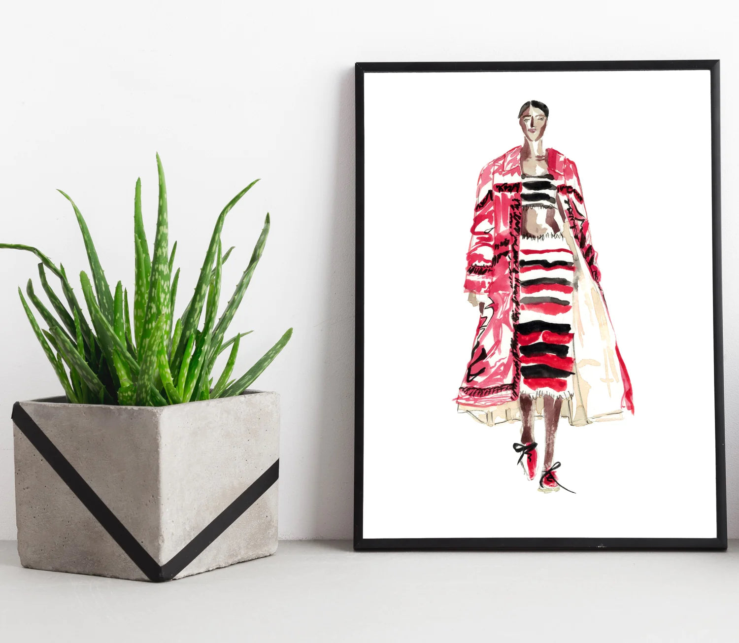 A framed fashion illustration print sits on a ledge next to a plant