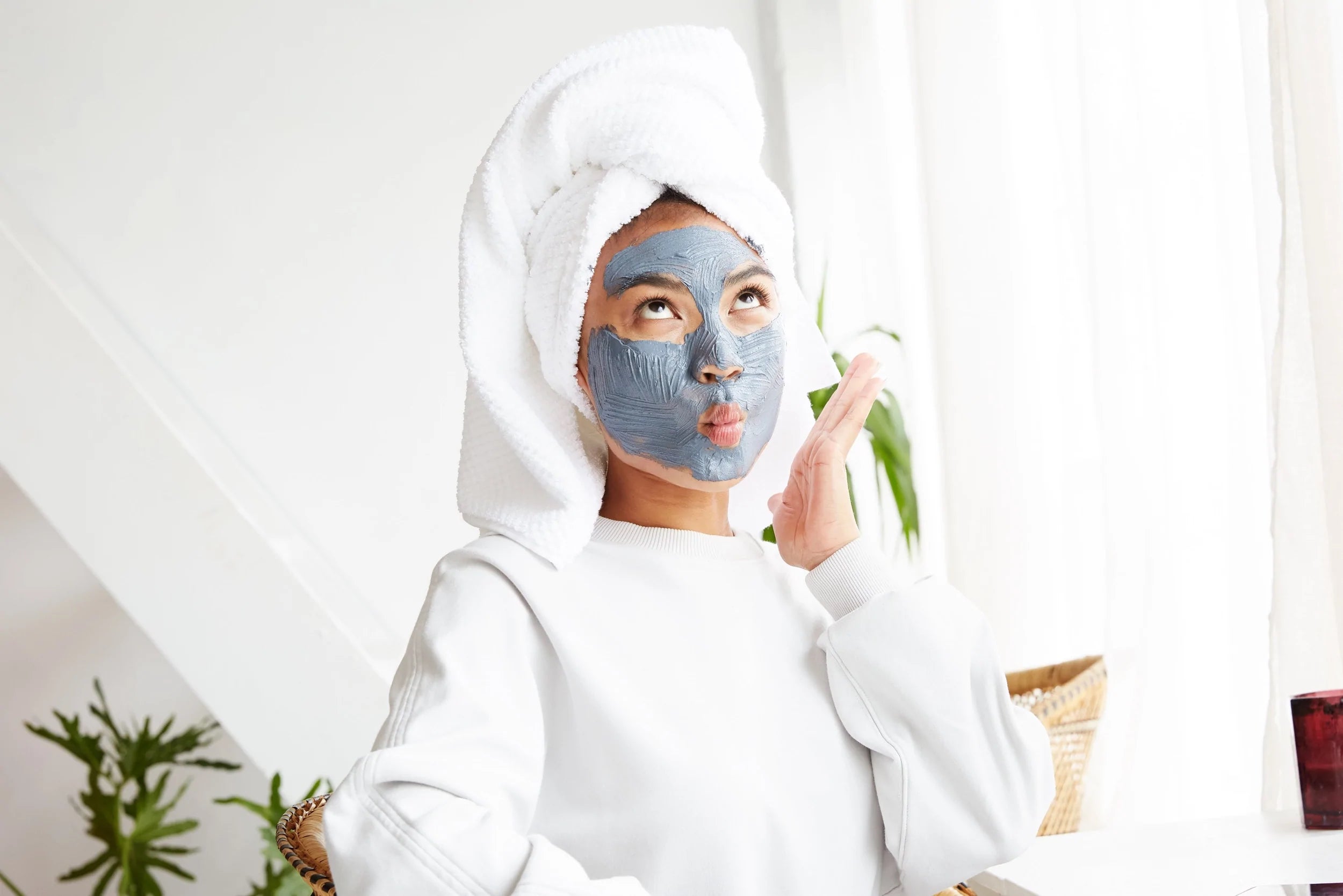 Person wearing a towel on their head and a clay face mask poses with a silly expression