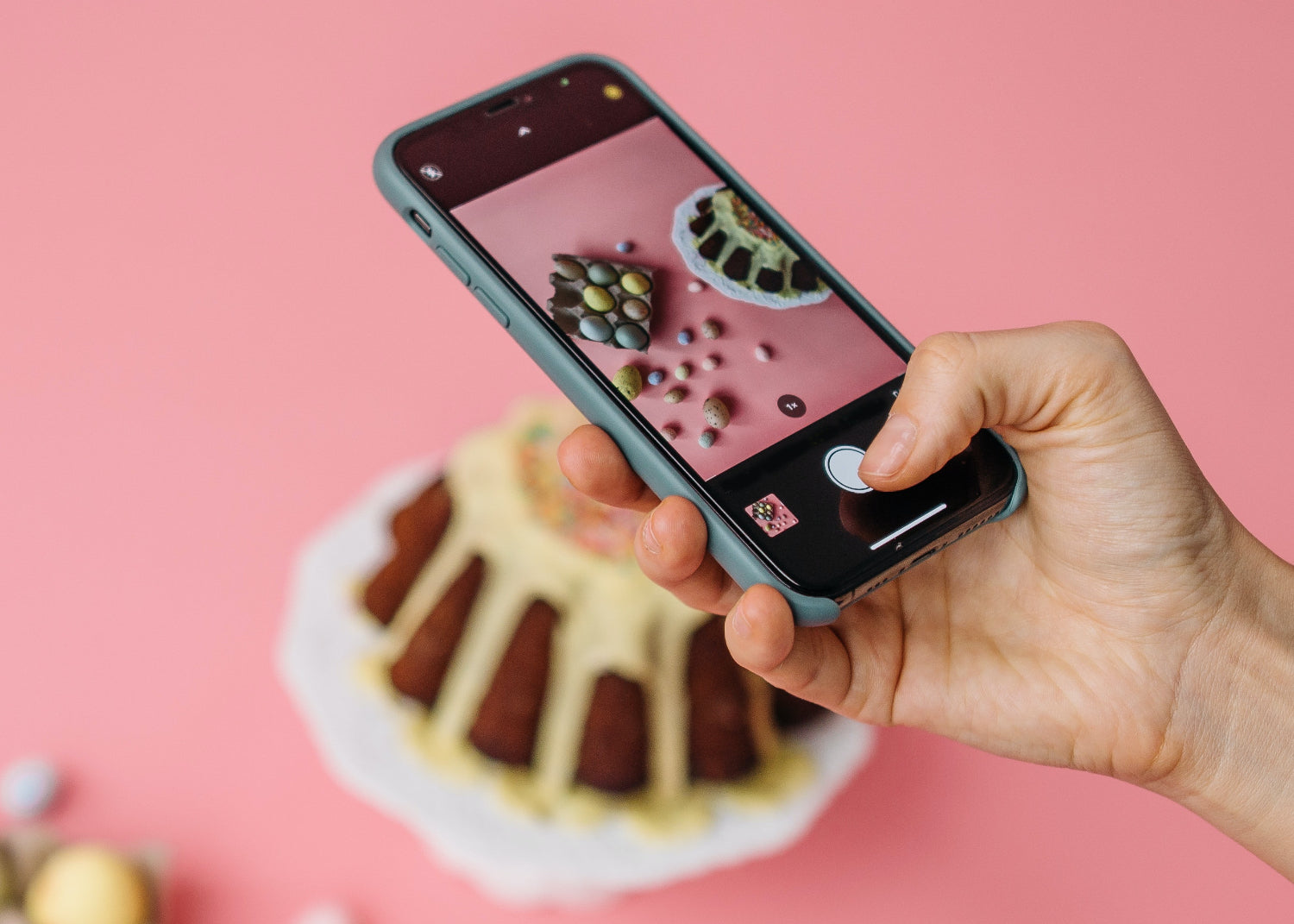 Close cropped image of a hand holding a mobile phone taking a photo of a cake