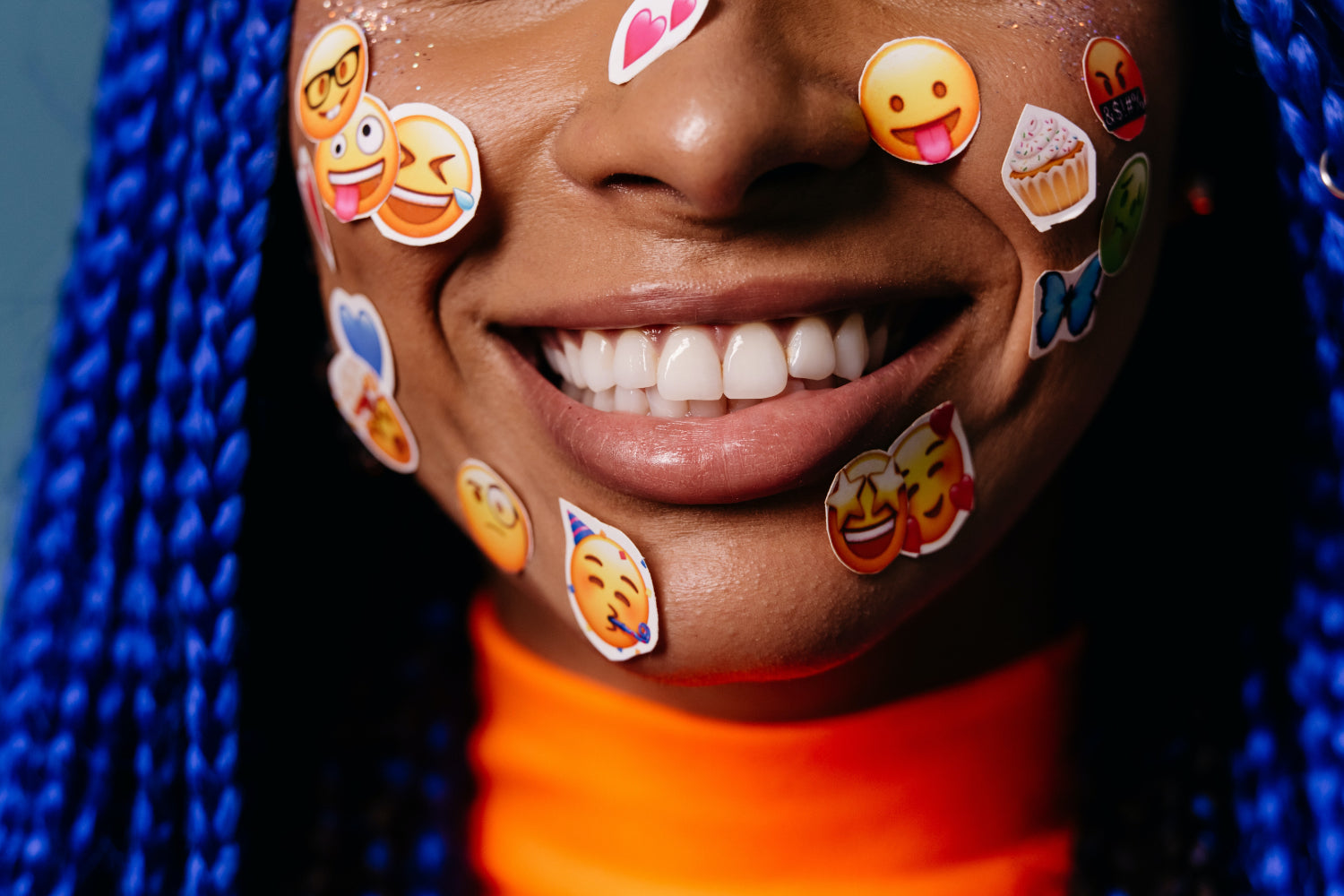 Woman with blue braids wears emoji stickers on her face