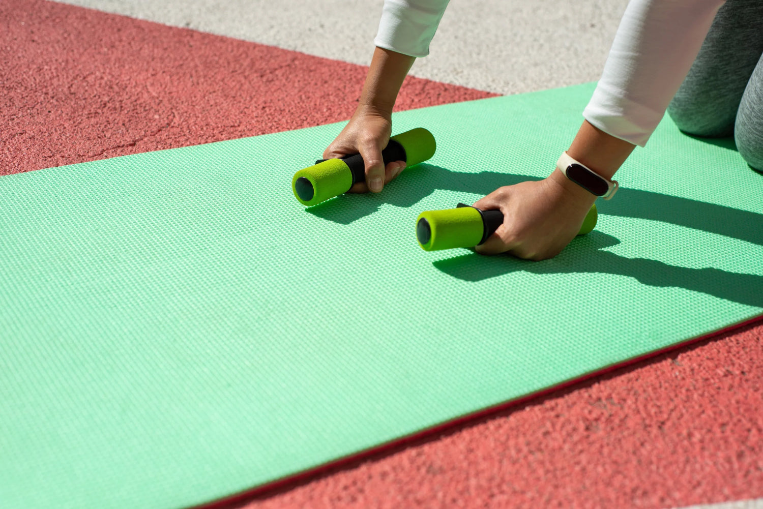 A person bends over a yoga mat holding small hand weights