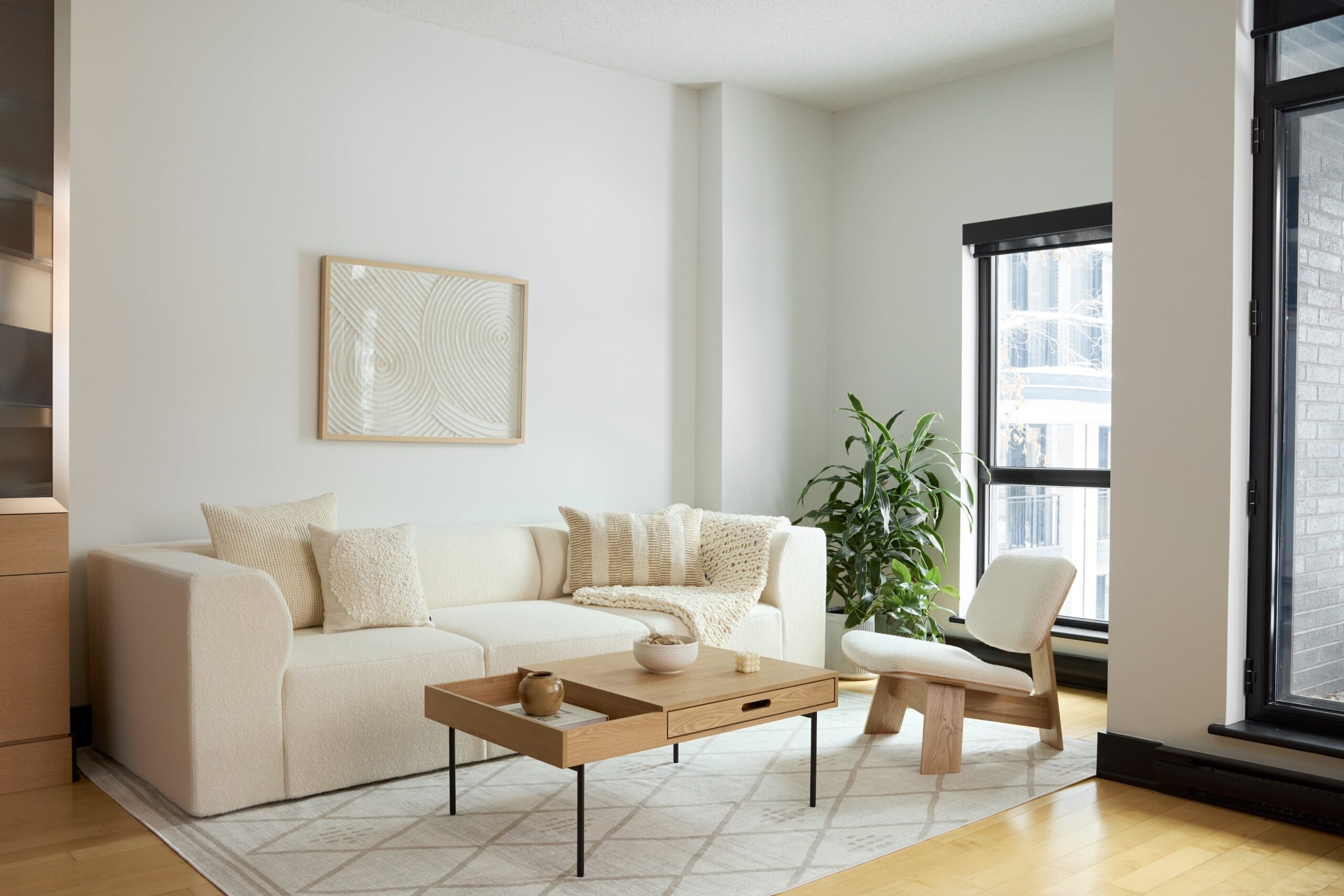 Attractively arranged Cozey couch, coffee table, chair, rug, and plant near light-filled windows.