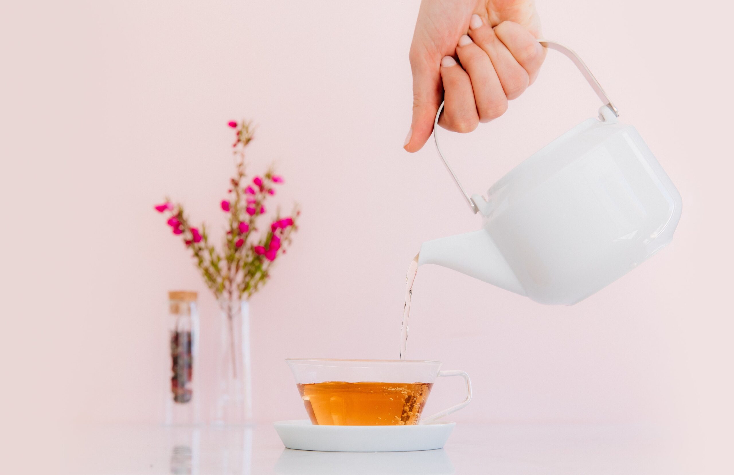 a hand pouring hot water out of a kettle into a teacup.