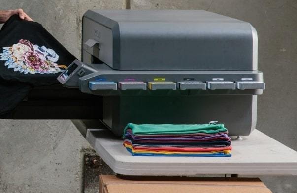 Black garment with a floral graphic being fed into a direct-to-garment printing machine.