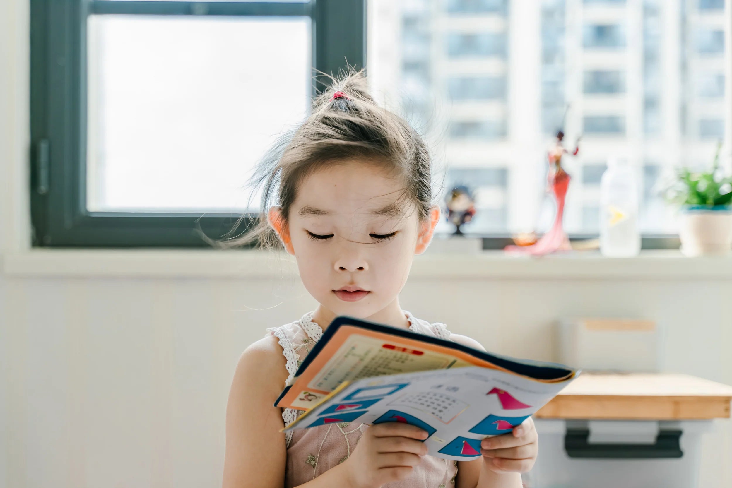 Child reads a book in front of a large window