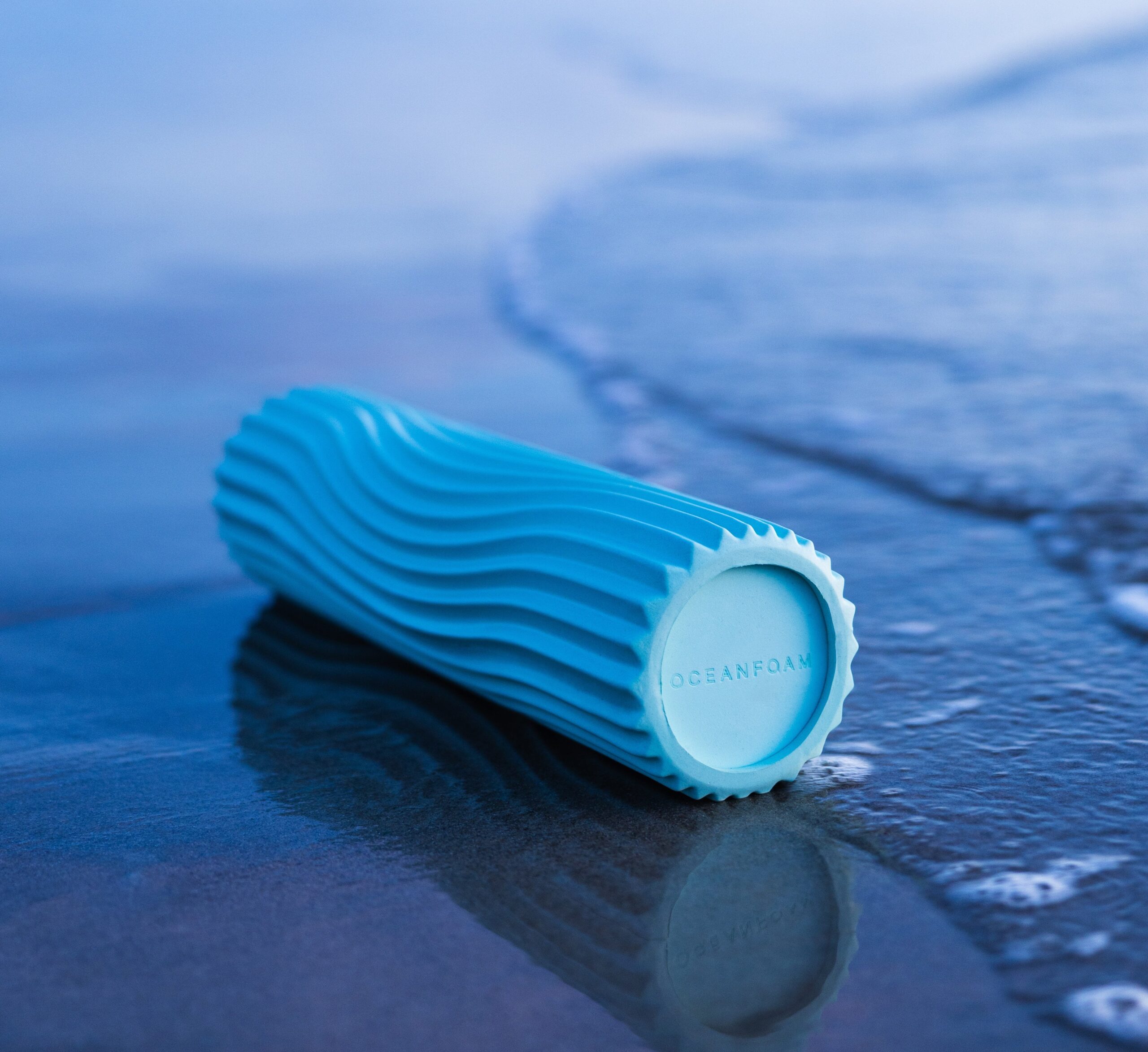 an oceanfoam roller laying in the sand where the waves crash on the beach.