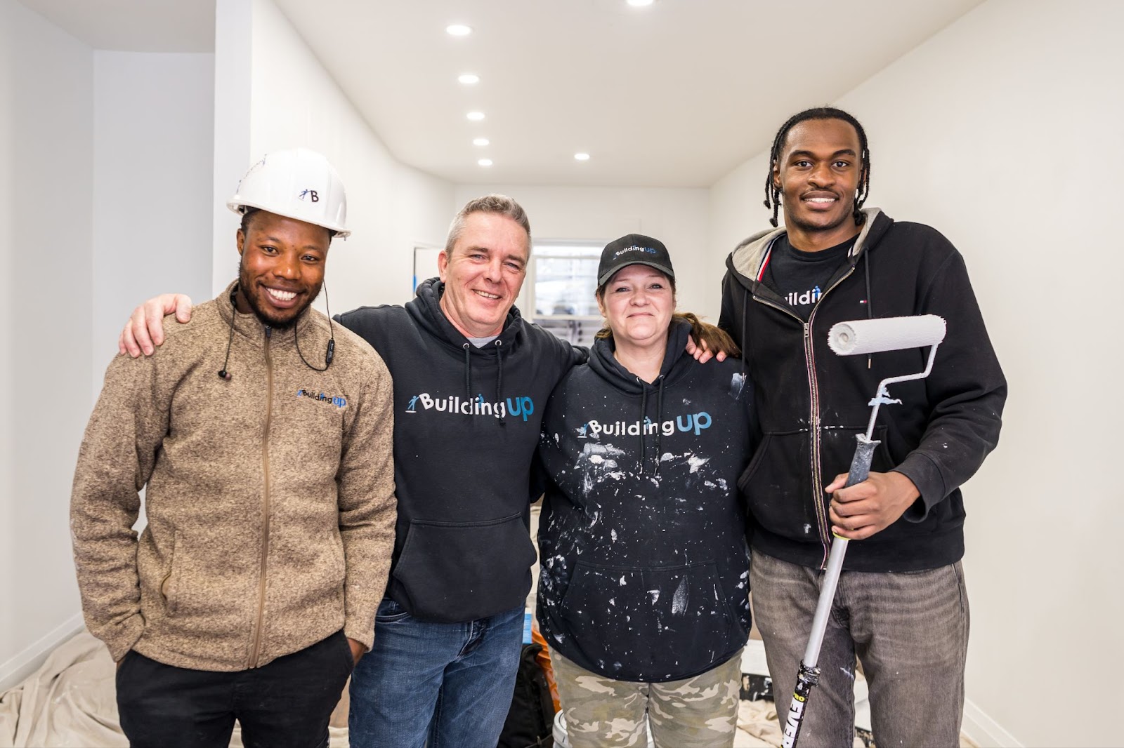 Four people standing together wearing shirts with the logo Building Up in the middle of a painting job. 