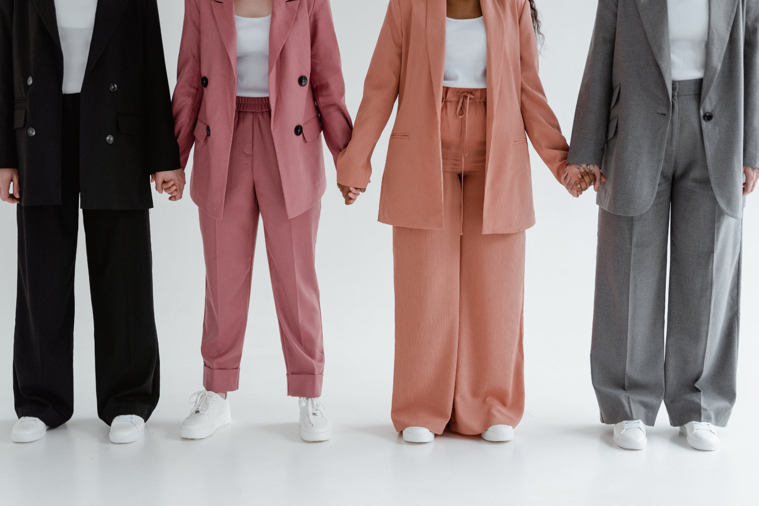 Four women, head out of frame, holding hands wearing pantsuits.