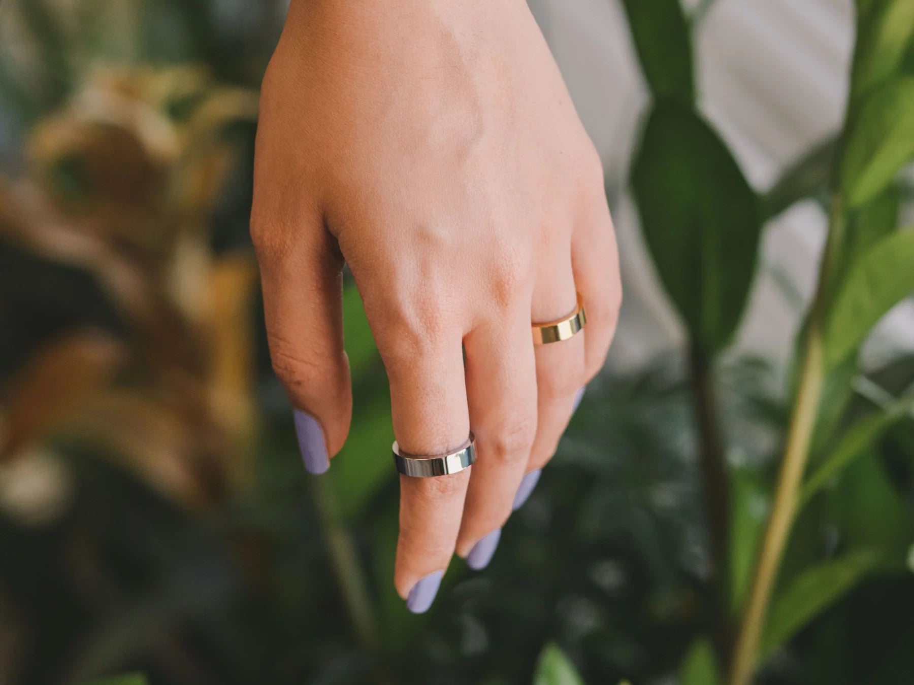 Hand wearing nail polish and Nominal jewelry silver and gold rings on index and ring fingers.