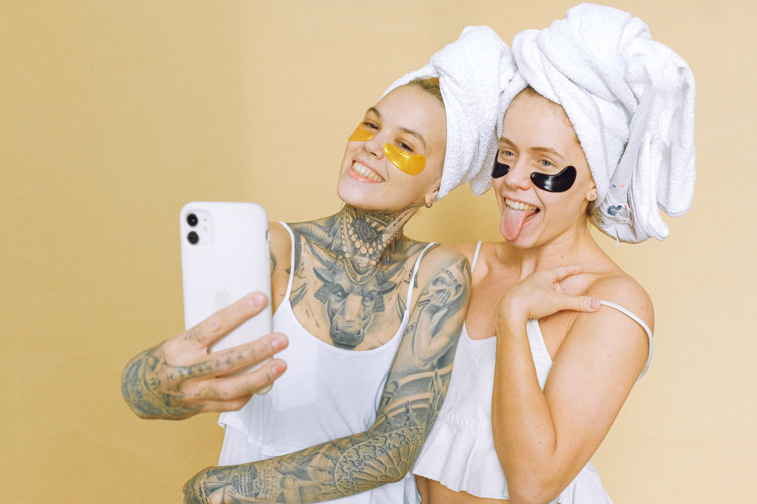 Two women with towels on their heads posing for a selfie while wearing under-eye masks.