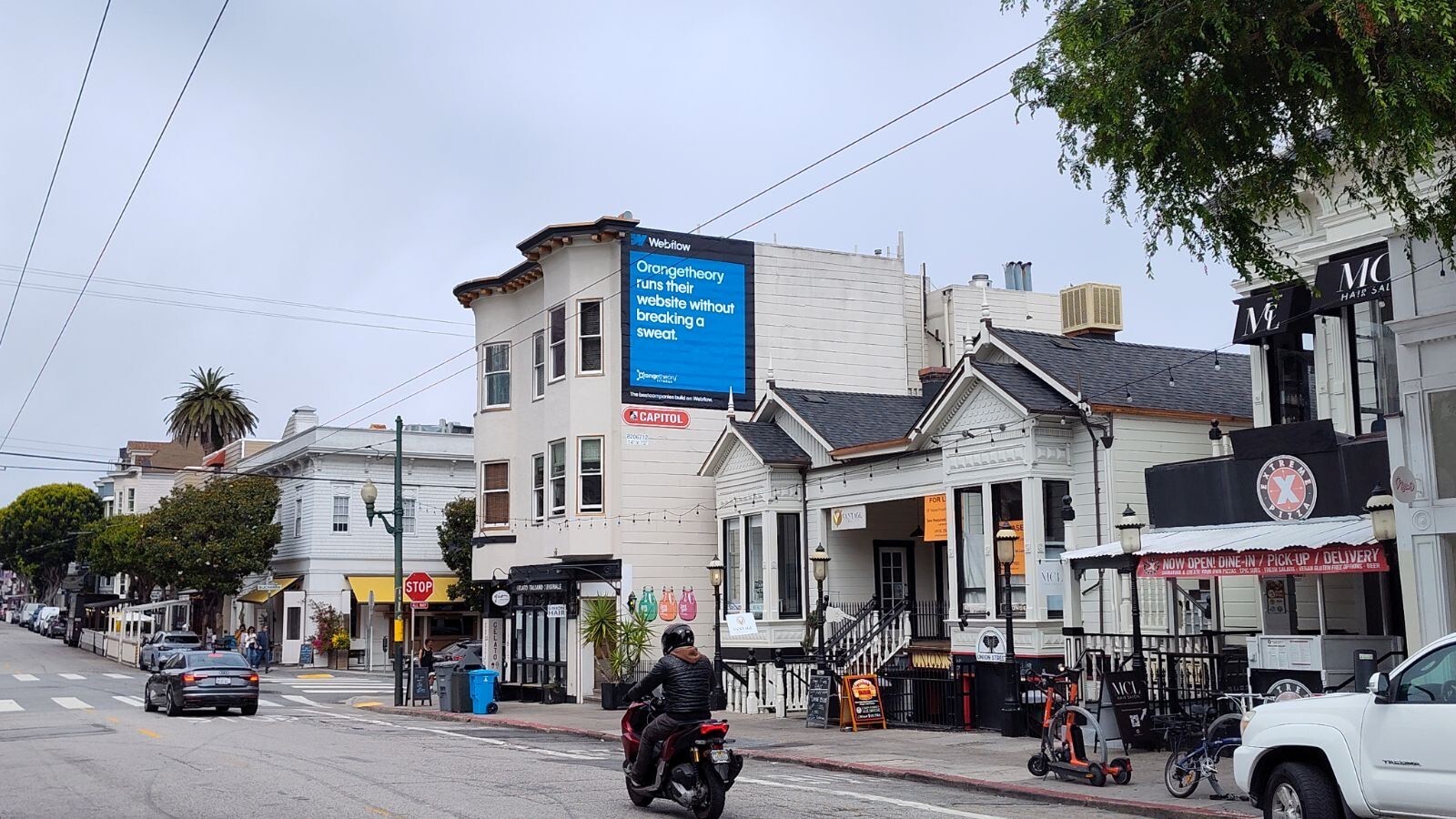 A photo of a street in San Francisco, including a row house with a blue banner ad on the side of it advertising Webflow.