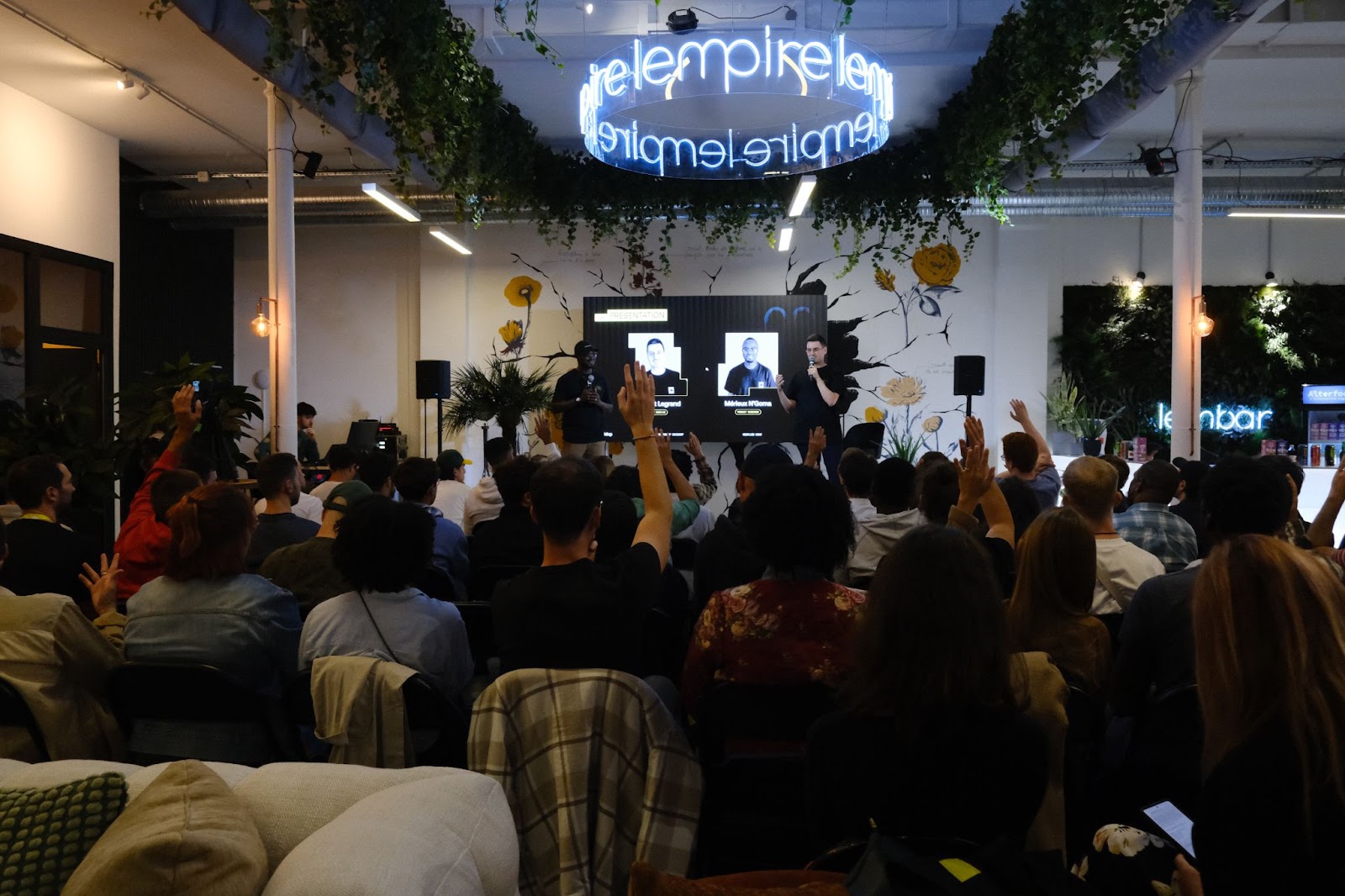 A community event in Hamburg, Germany. A full crowd with some people raising their hands to ask questions to two panelists on stage.