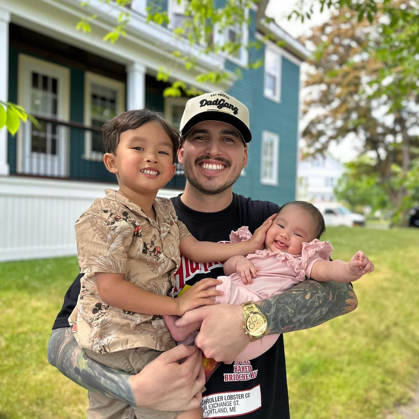 A dad wearing a Dad Gang Co hat while holding his two kids