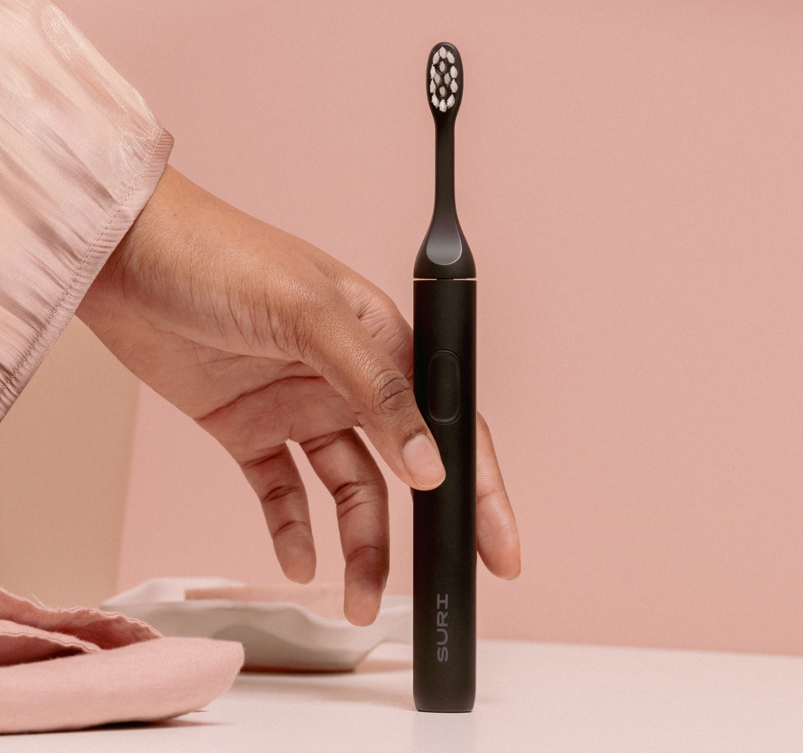 the SURI electric toothbrush with a model’s hand reaching to pick it up.