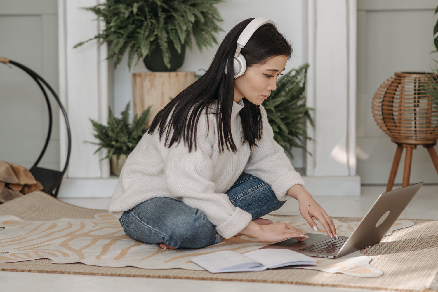 Woman with headphones sitting on a floor rug, working on a laptop.