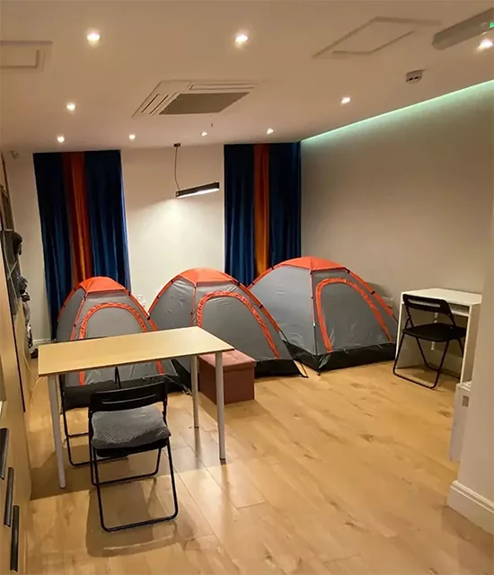 Three small tents set up in an indoor room with tables and chairs on a wooden floor.