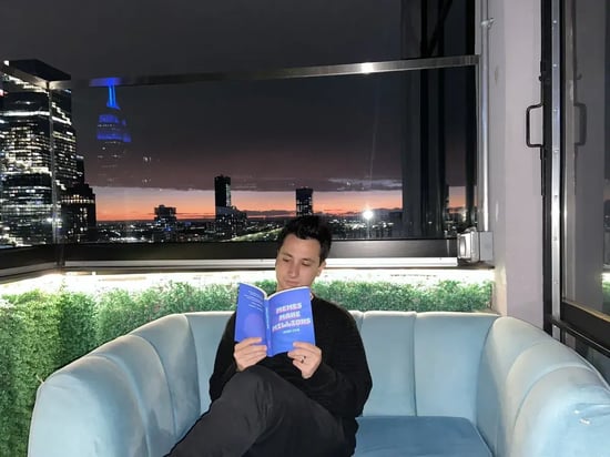 Jason Levin sitting on a couch reading his book, Memes Make Millions