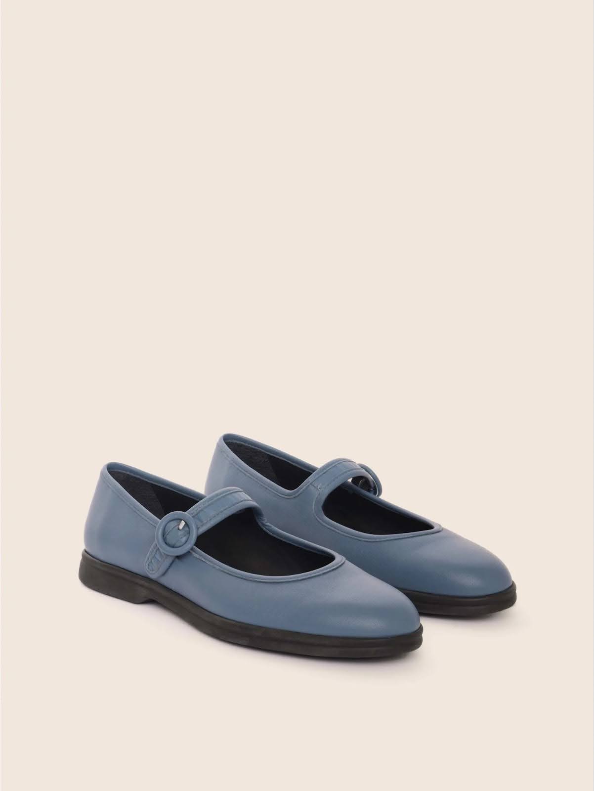 Blue Mary-Jane flats photographed at a 45-degree angle on an off-white background.