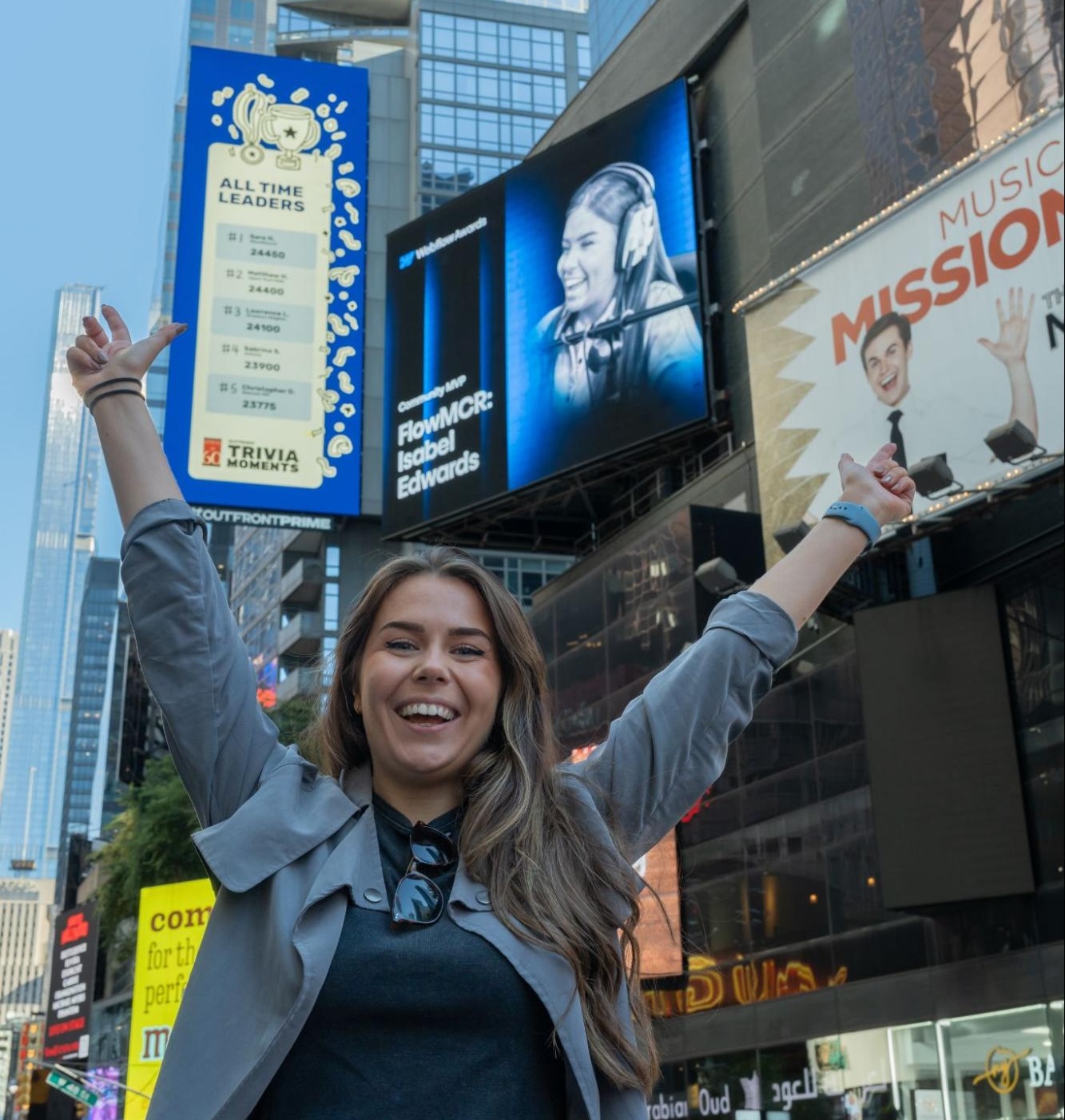 woman smiling with her arms raised in front of a billboard of her in times square