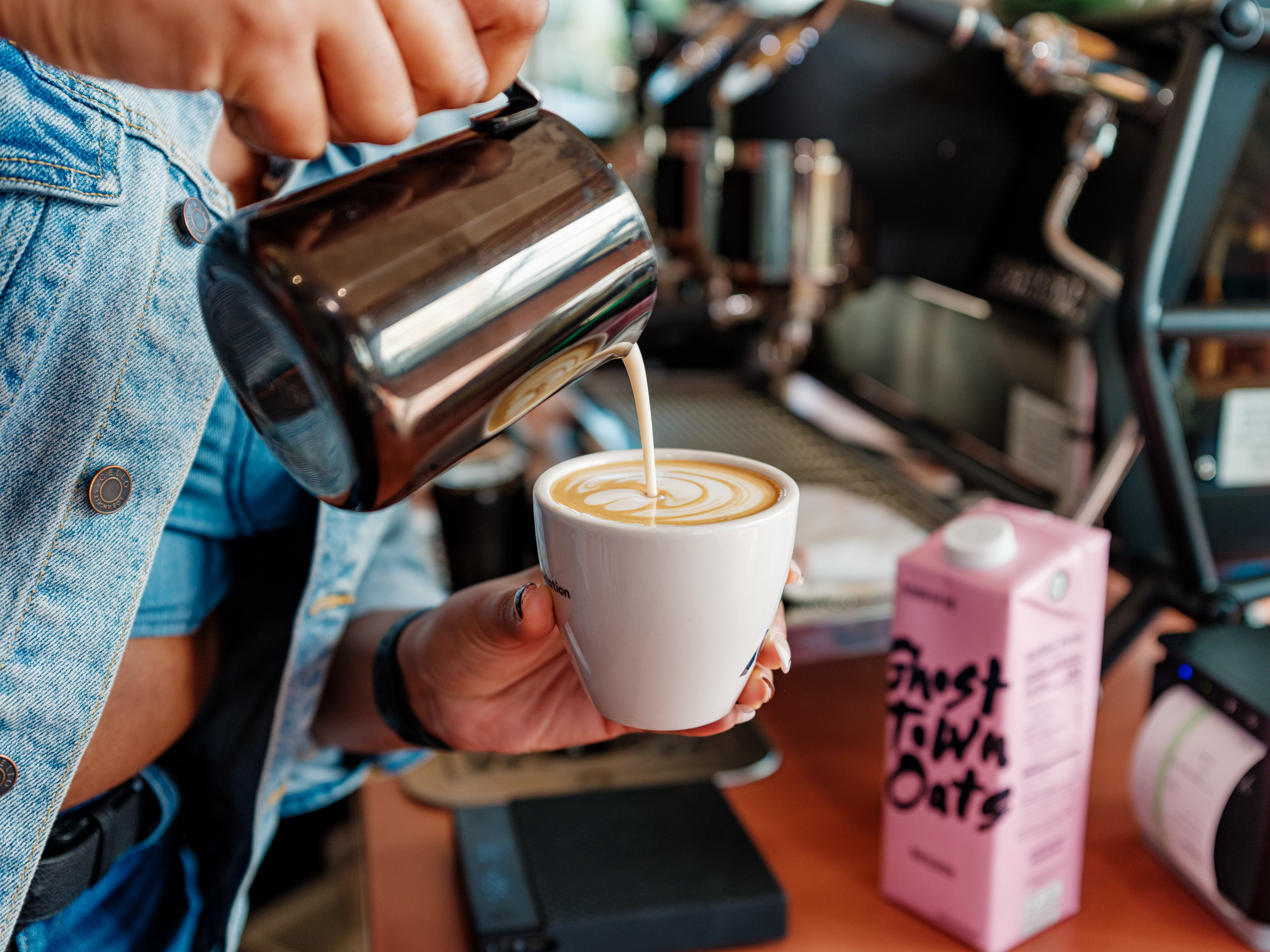 A model’s hand pours Ghost Town Oat milk into a coffee.