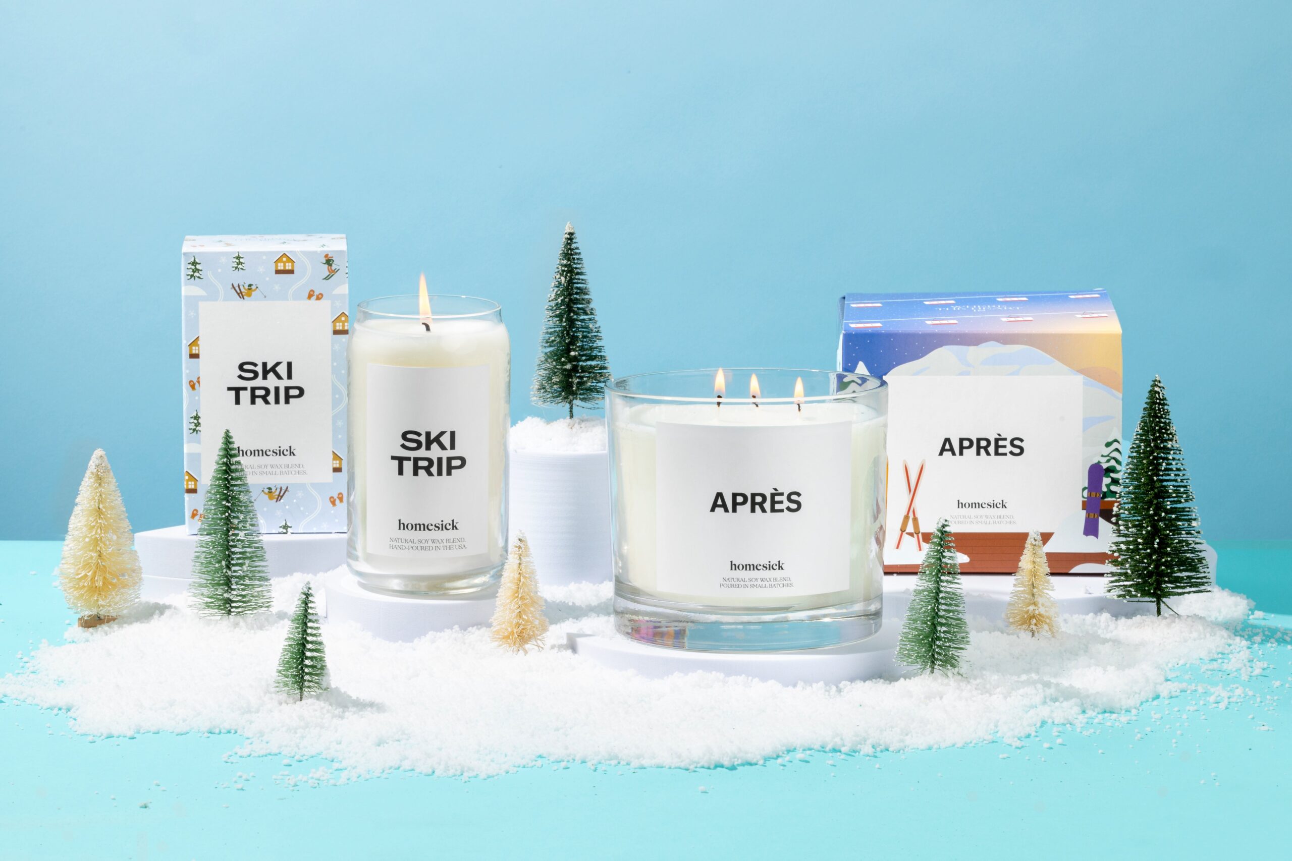 Homesick candles surrounded by snow and mini evergreen trees