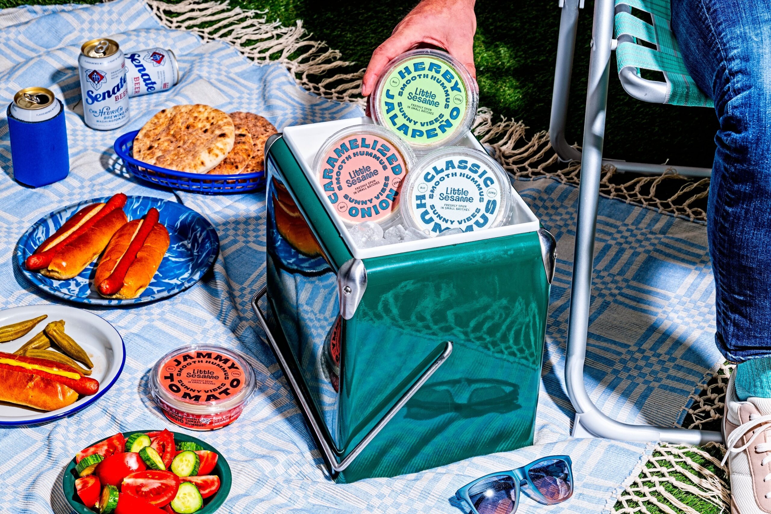 a picnic with food and drinks and a cooler of little sesame hummus in three different flavors.