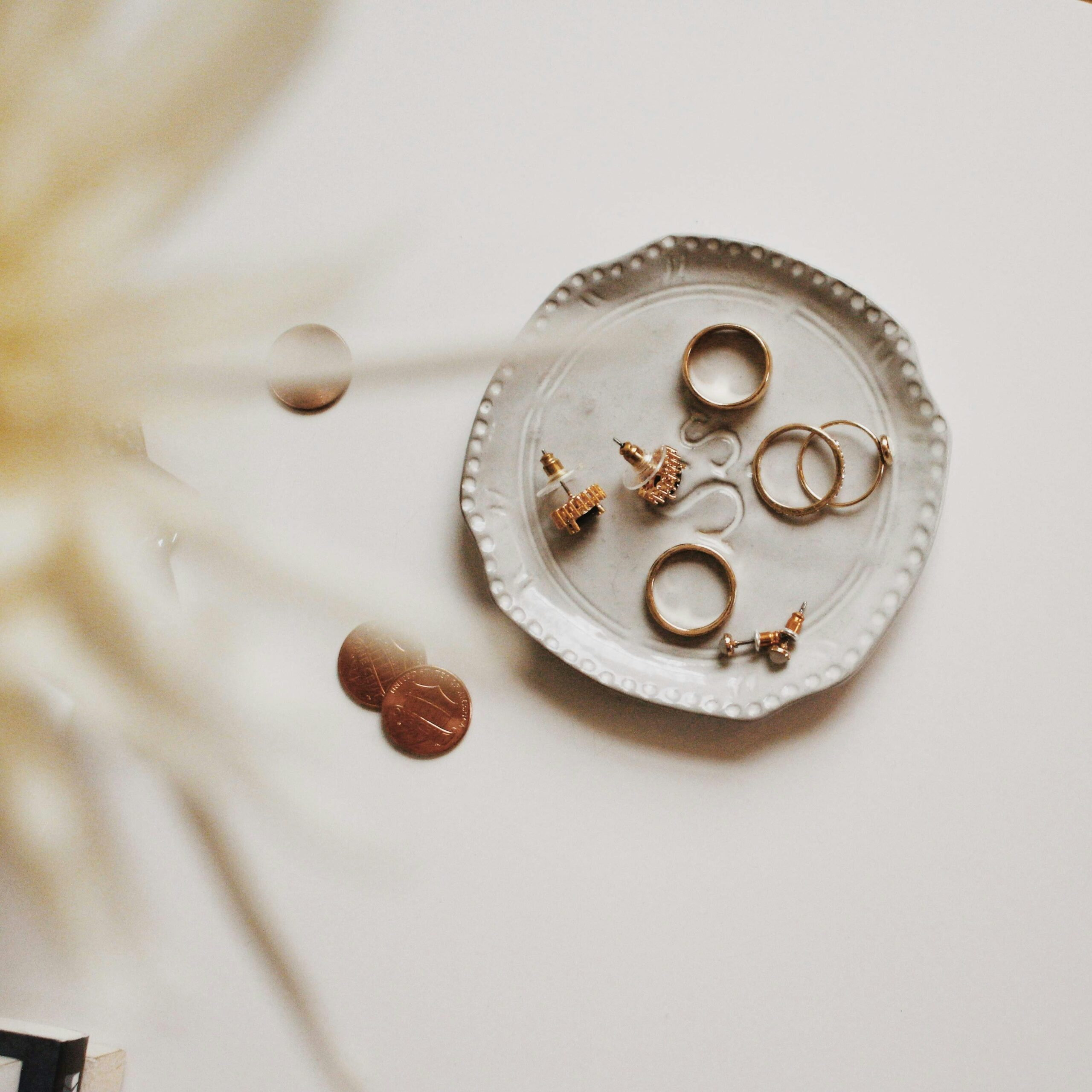 Jewelry sits in a cream dish next to pennies