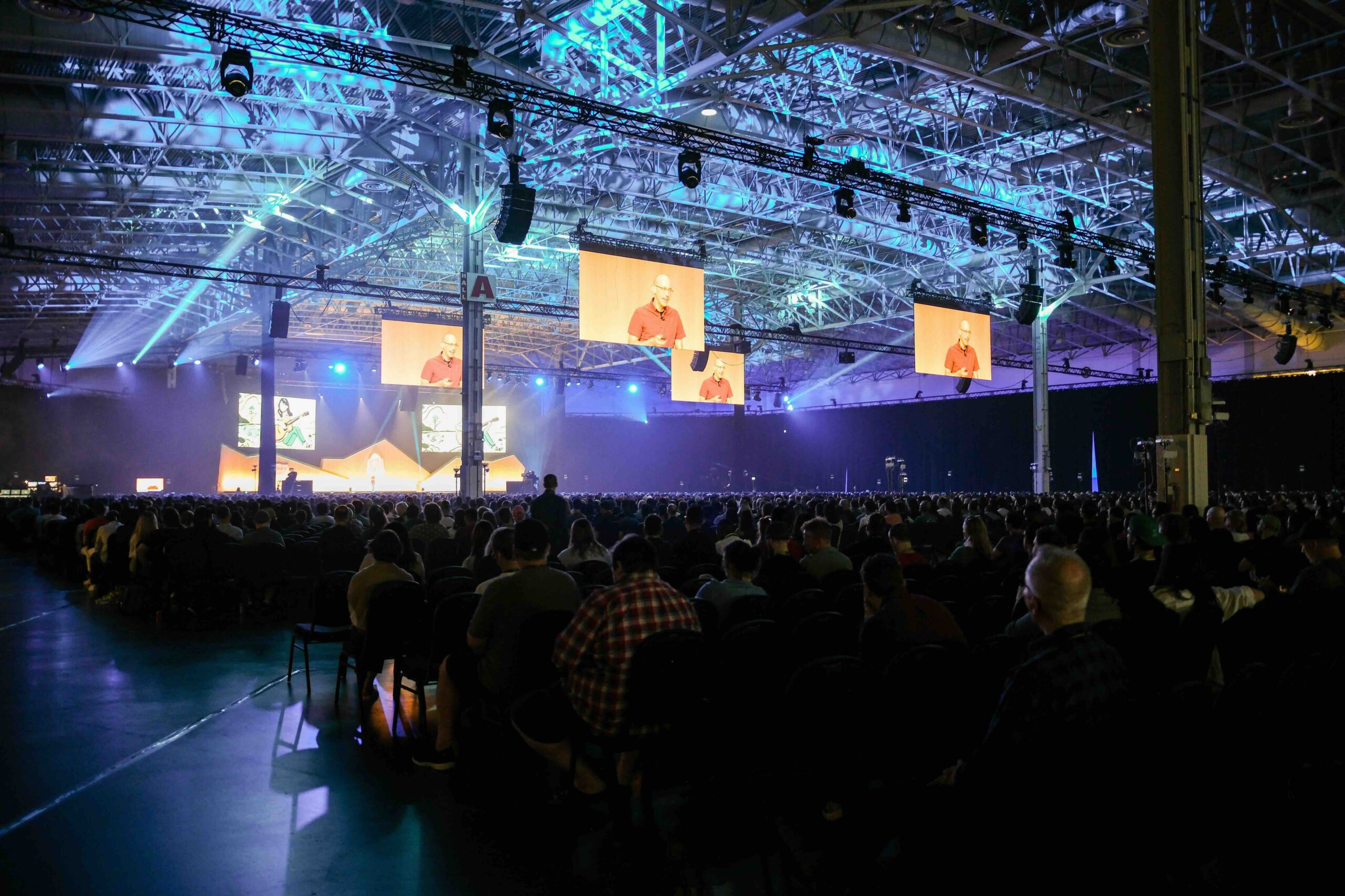 A crowd filled room with screens that display a speech given by Tobi Lütke.