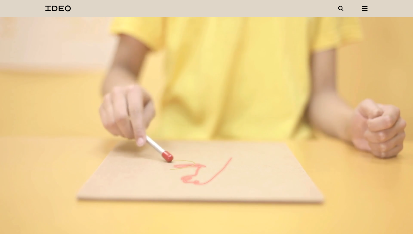 A screenshot of IDEO’s website with a beige header bar that contains a menu and search button in the top-right corner above a video loop.
