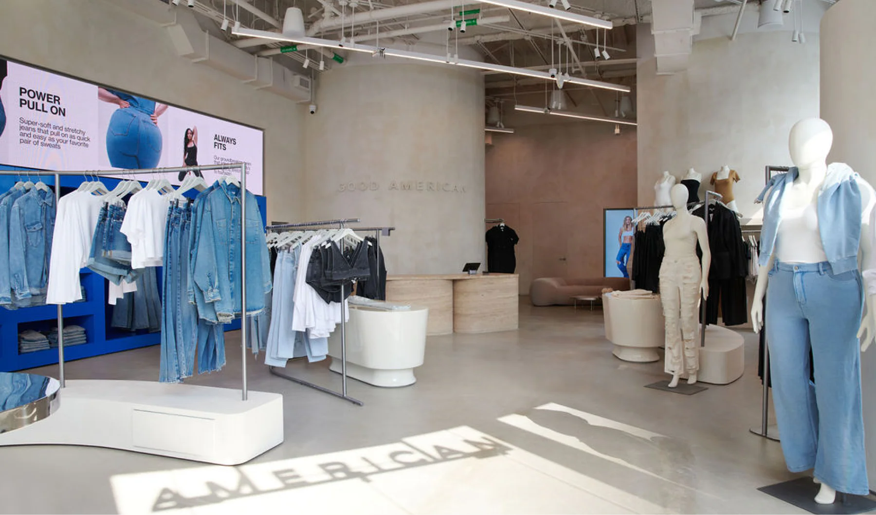 Good American’s retail store showing mannequins and digital screens next to clothing racks.
