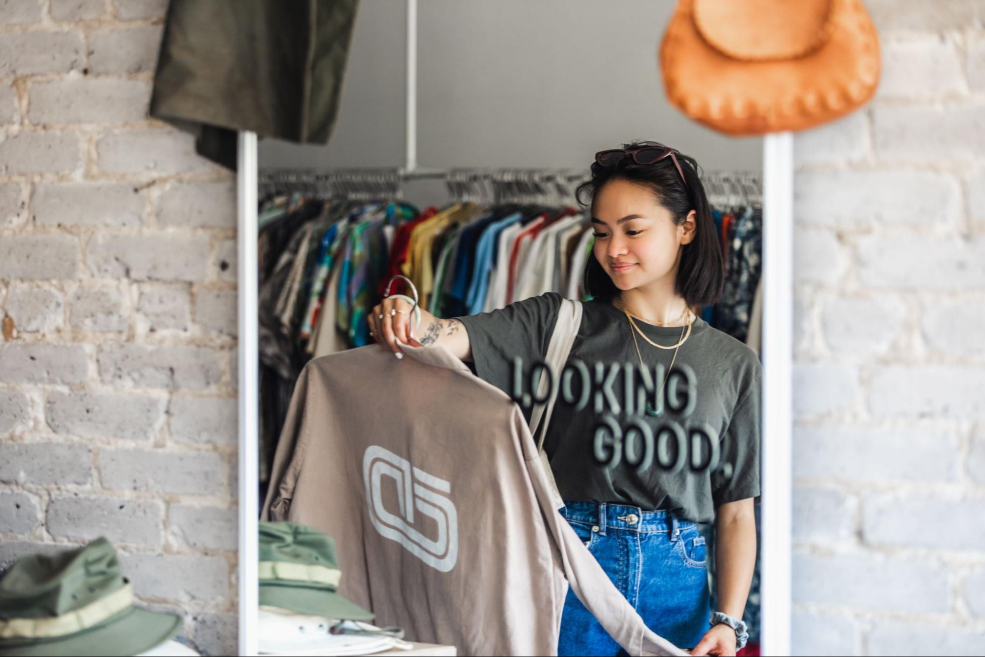 A view through a retail store mirror of a young woman shopping for clothes.