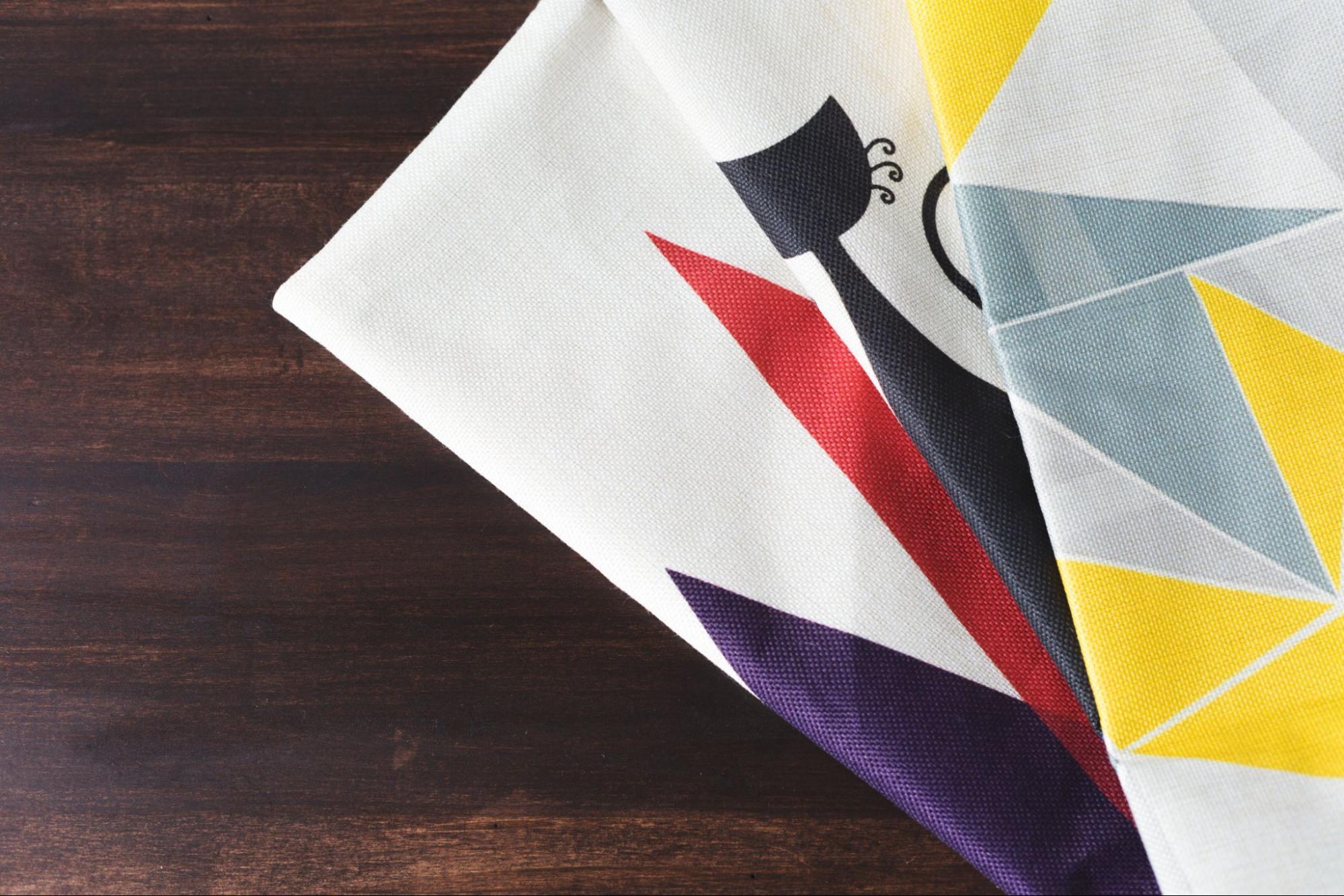 Three pieces of fabric with different geometric patterns sit on a wooden surface.