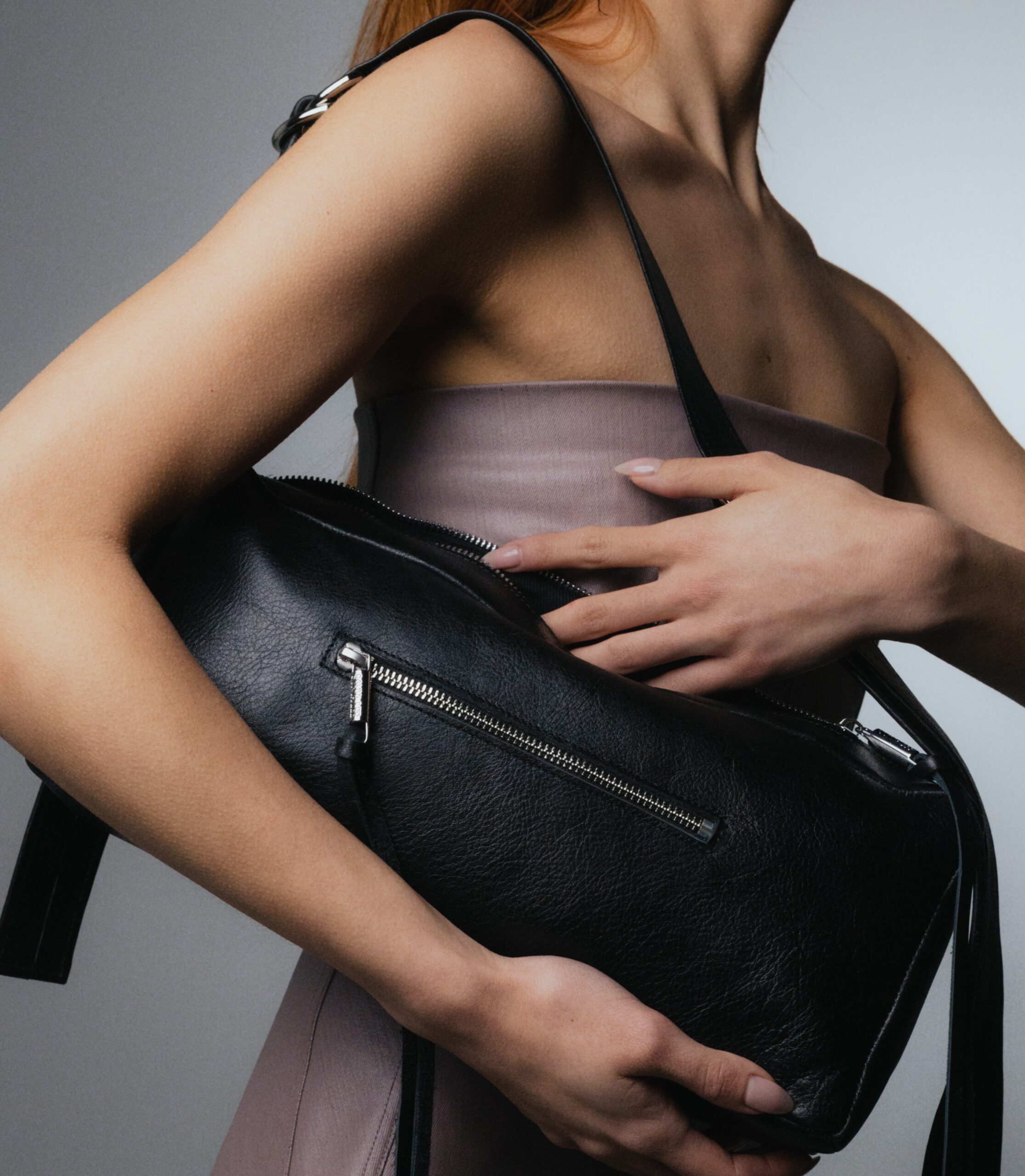 A model poses holding her Sonya Lee WINONA purse over her shoulder, with one hand under the bag, and another reaching inside.