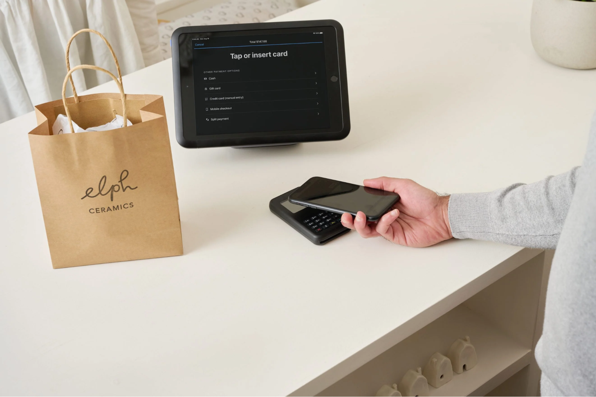 A customer makes a contactless payment with a phone at a shop counter.