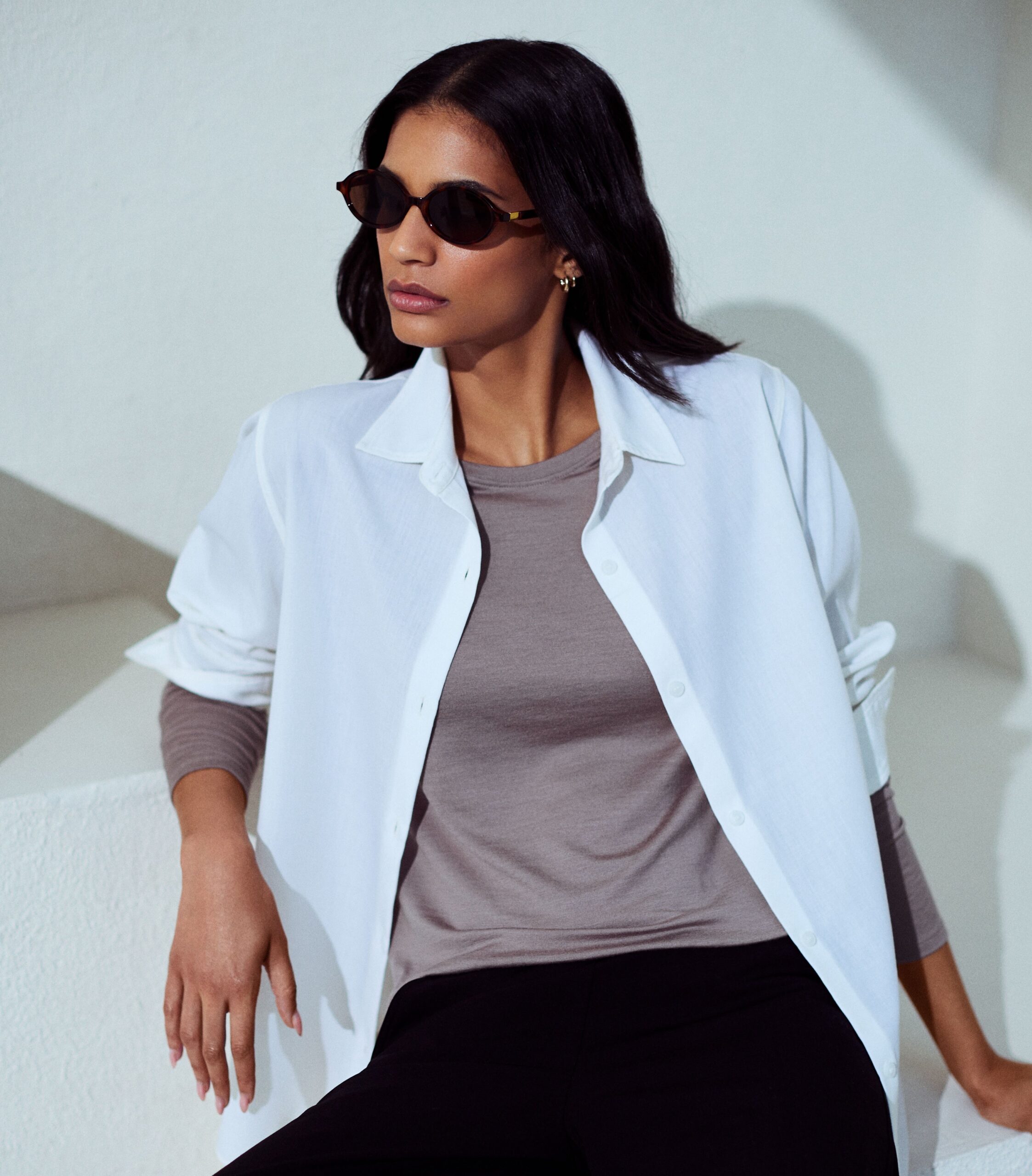 A model poses in a pair of sunglasses wearing Unbound Merino Women’s Long Sleeve Merino Crew Neck Fossil shirt.