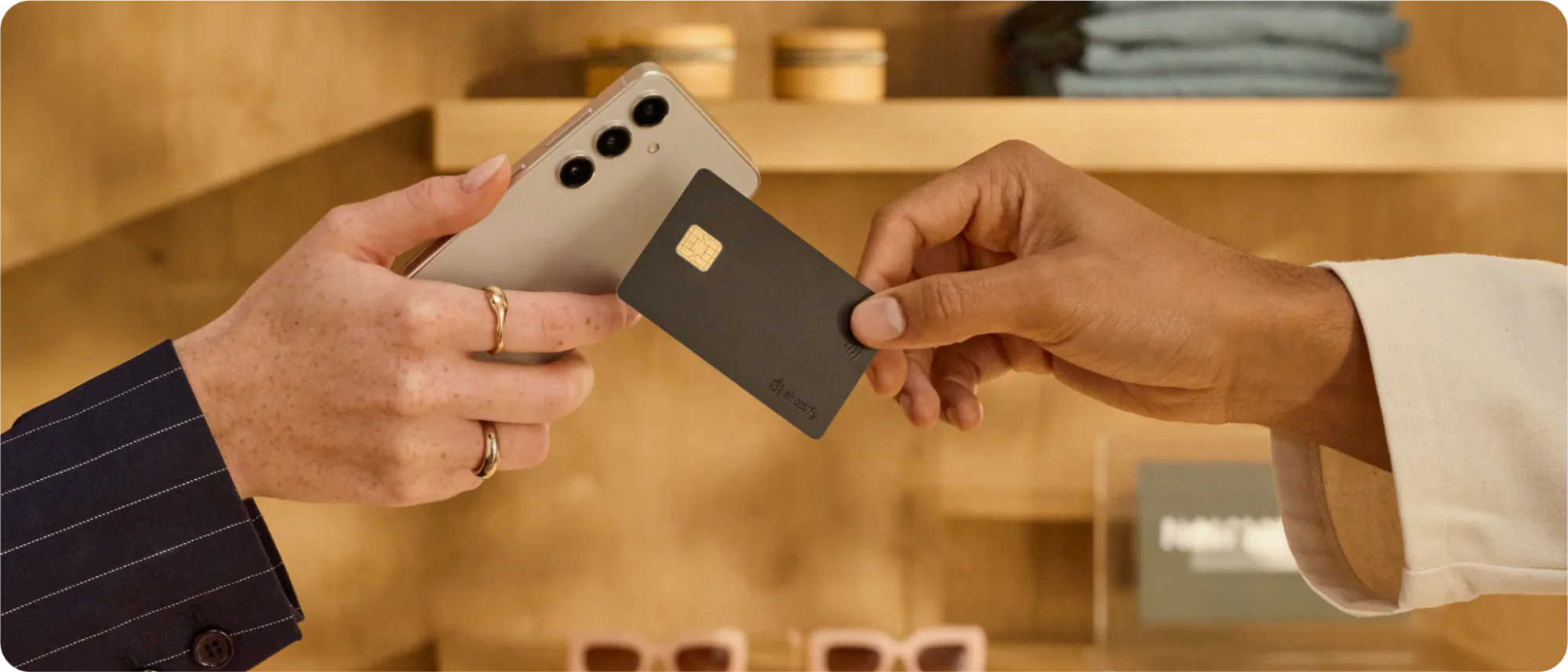 Person tapping a black credit card onto a silver iPhone in a clothing store.